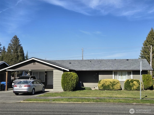 ranch-style house featuring aphalt driveway, an attached carport, a shingled roof, and a front lawn