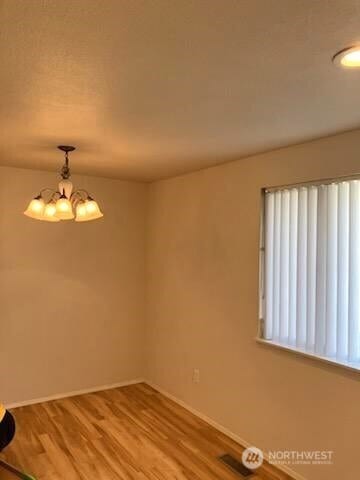 empty room with a notable chandelier, baseboards, and wood finished floors