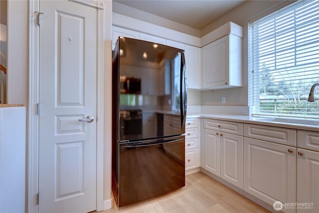 kitchen featuring light wood-style flooring, a sink, white cabinetry, freestanding refrigerator, and light countertops