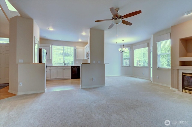 unfurnished living room featuring light carpet, ceiling fan with notable chandelier, a sink, a fireplace, and baseboards