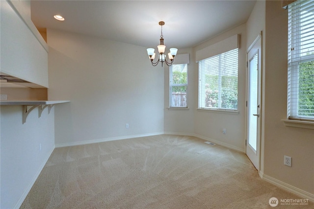 unfurnished dining area with a wealth of natural light, a notable chandelier, light colored carpet, and baseboards