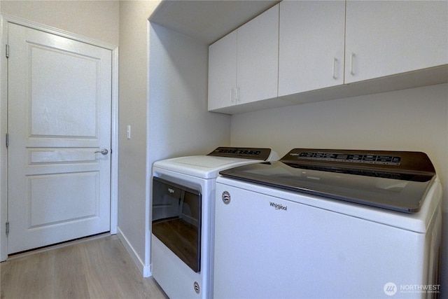 laundry area featuring washing machine and clothes dryer, cabinet space, light wood-type flooring, and baseboards