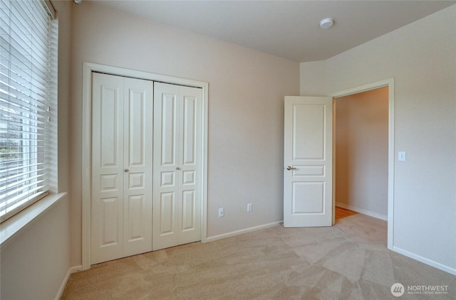 unfurnished bedroom featuring a closet, baseboards, and light colored carpet