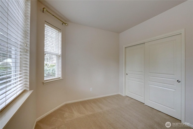 unfurnished bedroom featuring light carpet, a closet, and baseboards