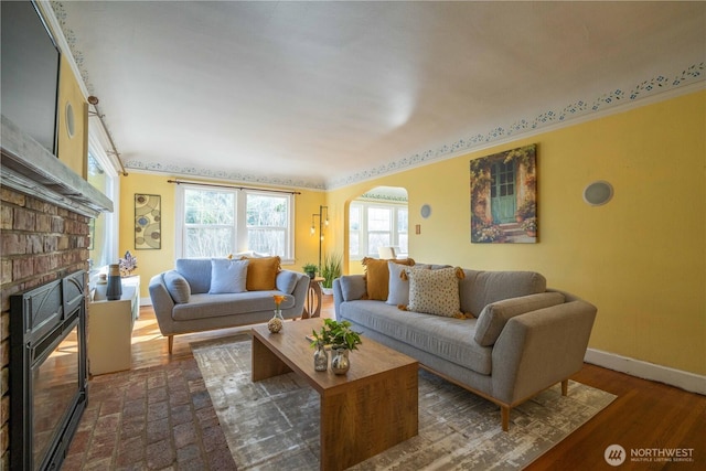 living room featuring arched walkways, crown molding, dark wood finished floors, a fireplace, and baseboards