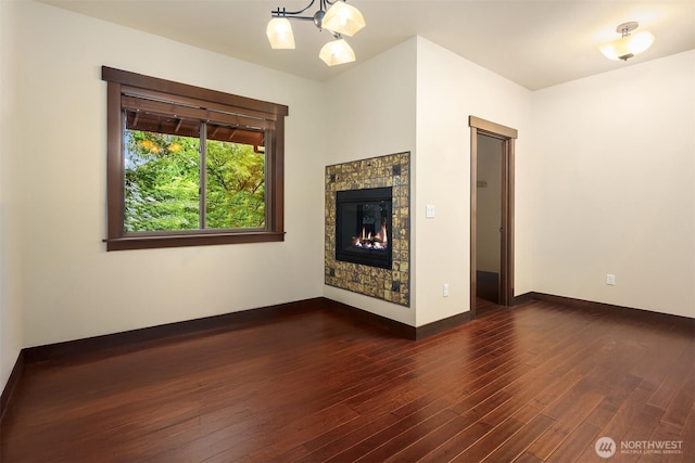 unfurnished living room featuring dark wood-style floors, a warm lit fireplace, and baseboards