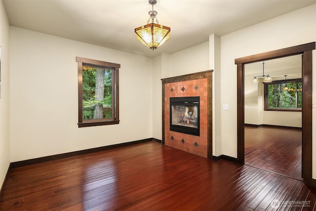 empty room with a tile fireplace, wood finished floors, a wealth of natural light, and baseboards