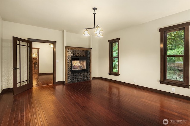 unfurnished living room featuring a glass covered fireplace, an inviting chandelier, baseboards, and hardwood / wood-style flooring