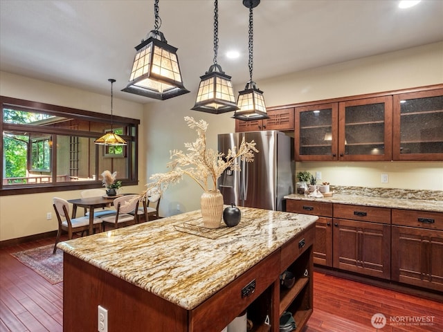 kitchen featuring hanging light fixtures, light stone counters, dark wood finished floors, and freestanding refrigerator