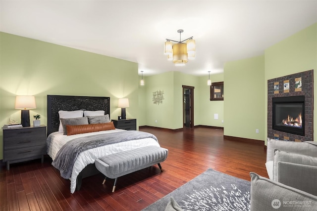 bedroom featuring a tiled fireplace, wood finished floors, an inviting chandelier, and baseboards