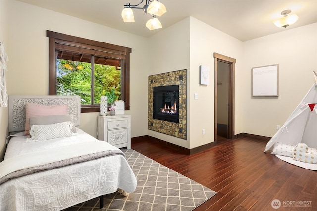 bedroom featuring a chandelier, a fireplace, baseboards, and wood finished floors