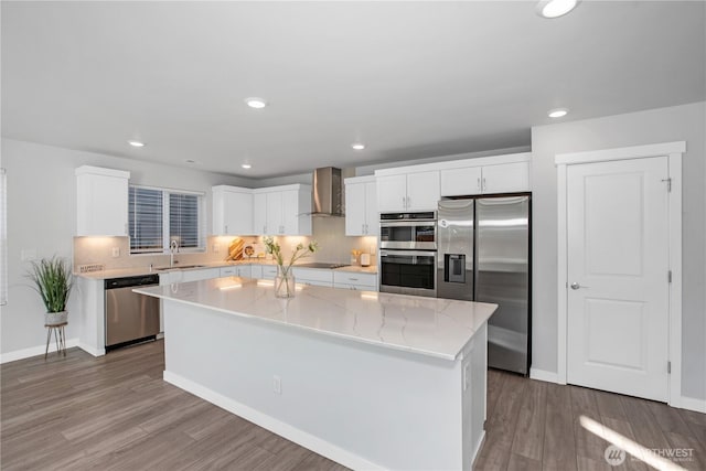 kitchen featuring appliances with stainless steel finishes, a sink, wall chimney range hood, and wood finished floors