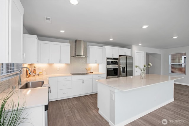 kitchen with wall chimney exhaust hood, appliances with stainless steel finishes, a sink, and wood finished floors