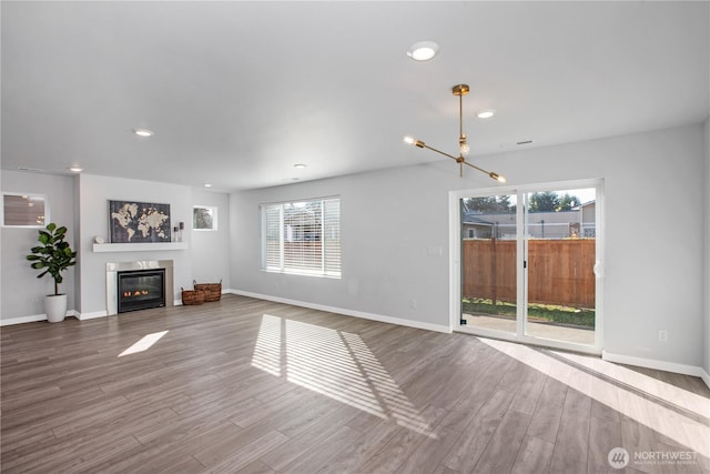 unfurnished living room with baseboards, wood finished floors, and a glass covered fireplace