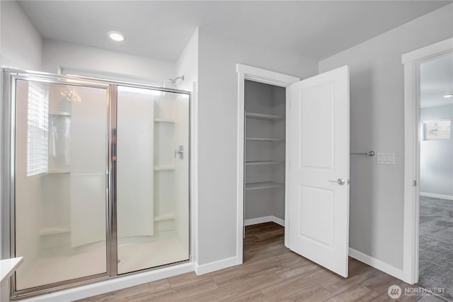 bathroom featuring a stall shower, a spacious closet, baseboards, and wood finished floors