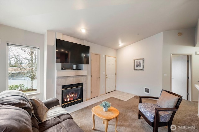 living room featuring visible vents, lofted ceiling, light colored carpet, and a tile fireplace