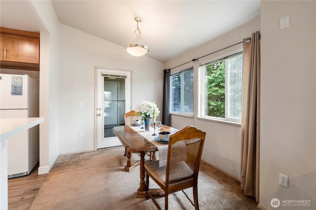 dining room featuring baseboards, light colored carpet, and vaulted ceiling