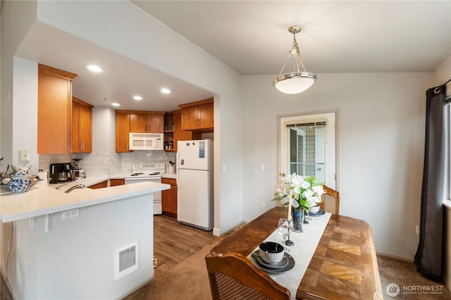 kitchen featuring visible vents, white appliances, a peninsula, light countertops, and decorative backsplash