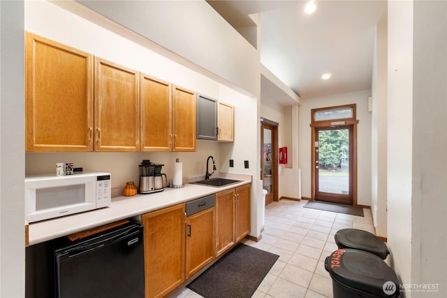 kitchen with white microwave, light countertops, light tile patterned floors, dishwashing machine, and a sink