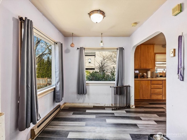 unfurnished dining area with arched walkways, dark wood-style flooring, baseboard heating, and a healthy amount of sunlight