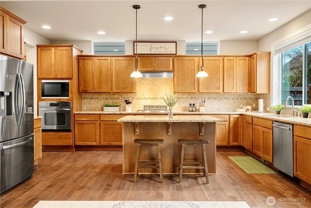 kitchen with under cabinet range hood, appliances with stainless steel finishes, wood finished floors, and a sink