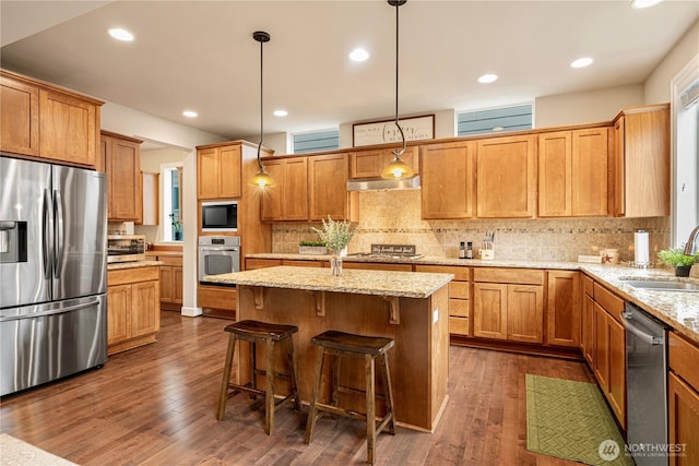 kitchen with pendant lighting, a sink, dark wood-style floors, appliances with stainless steel finishes, and light stone countertops