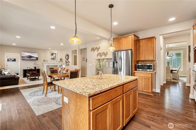 kitchen with a kitchen island, dark wood-type flooring, light stone countertops, a tile fireplace, and stainless steel appliances