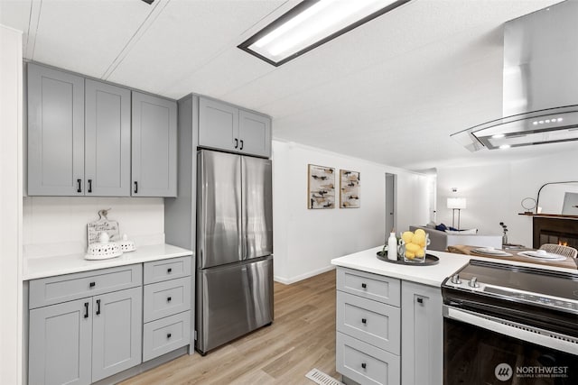 kitchen with wall chimney range hood, stainless steel fridge, gray cabinetry, and electric stove