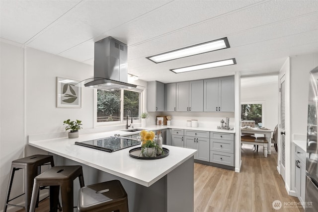 kitchen with gray cabinetry, a breakfast bar, stovetop, a peninsula, and island range hood