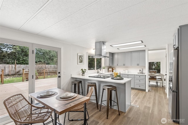 kitchen featuring light wood-type flooring, gray cabinets, island exhaust hood, a peninsula, and light countertops