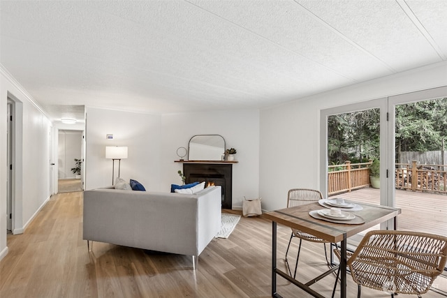 living room featuring light wood-type flooring, a textured ceiling, and a warm lit fireplace