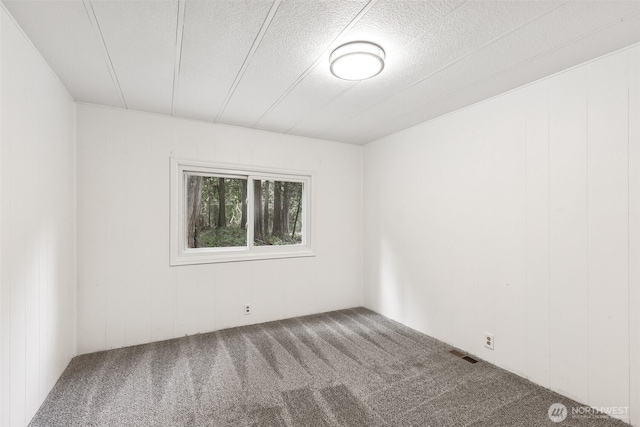 empty room with carpet, visible vents, and a textured ceiling