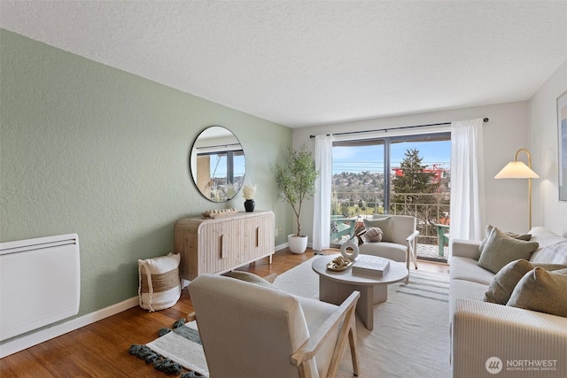 living area with a textured ceiling, a textured wall, wood finished floors, and baseboards