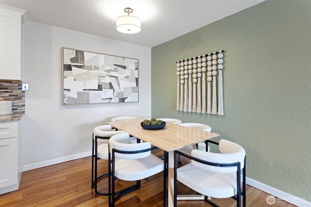 dining space with baseboards, wood finished floors, and a textured wall