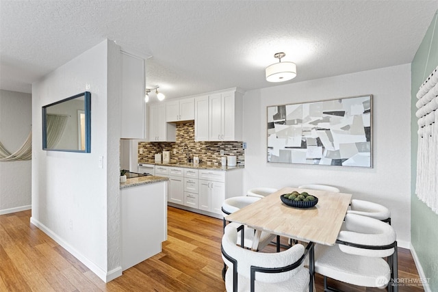 kitchen featuring a textured ceiling, tasteful backsplash, white cabinetry, and light wood-style floors