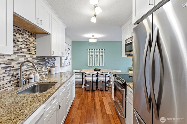 kitchen featuring stainless steel appliances, wood finished floors, a sink, and white cabinetry