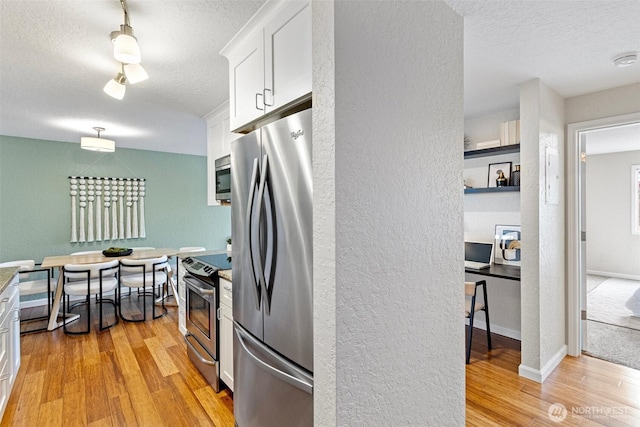 kitchen featuring a textured ceiling, light wood-style flooring, white cabinetry, baseboards, and appliances with stainless steel finishes