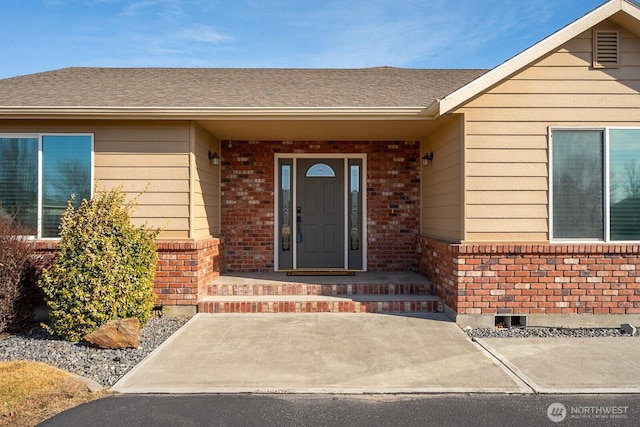 view of exterior entry with roof with shingles and brick siding