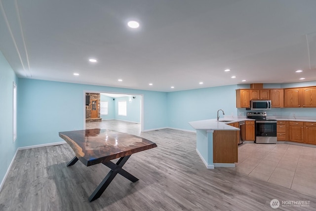 kitchen featuring recessed lighting, stainless steel appliances, a peninsula, a sink, and light countertops