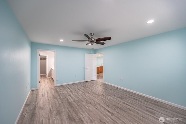 unfurnished bedroom featuring a walk in closet, recessed lighting, a ceiling fan, wood finished floors, and baseboards