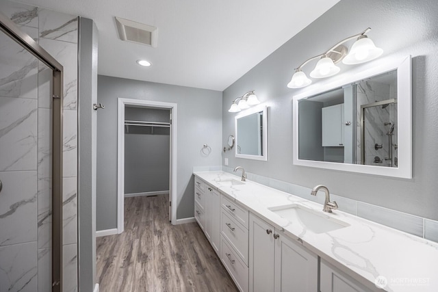 bathroom with a marble finish shower, visible vents, wood finished floors, a spacious closet, and a sink