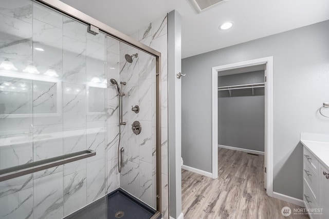 full bathroom featuring a walk in closet, a marble finish shower, visible vents, wood finished floors, and baseboards