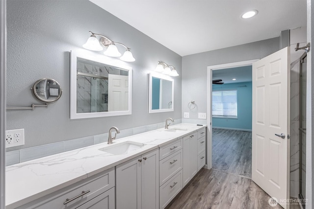 full bathroom with double vanity, an enclosed shower, a sink, and wood finished floors