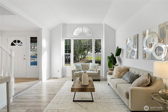 living room featuring vaulted ceiling, stairway, baseboards, and light wood-style floors