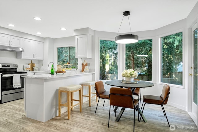 kitchen with light wood-style flooring, under cabinet range hood, a peninsula, white cabinets, and stainless steel range with electric cooktop