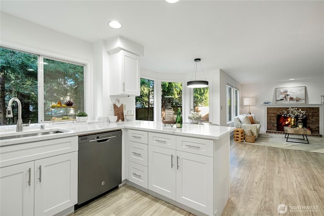 kitchen with a fireplace, a sink, light wood-type flooring, dishwasher, and a peninsula