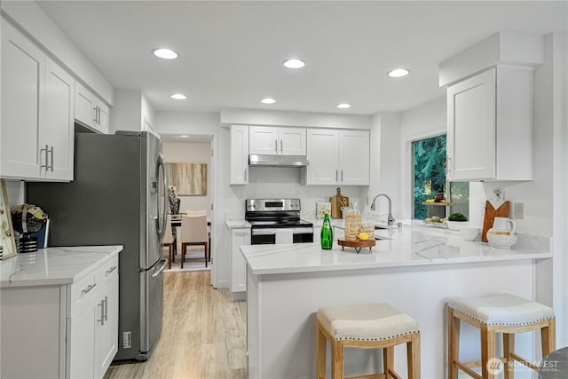 kitchen with a breakfast bar, stainless steel appliances, white cabinetry, a peninsula, and under cabinet range hood