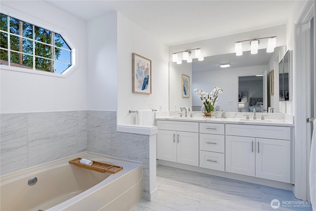 bathroom featuring a bath, marble finish floor, double vanity, and a sink