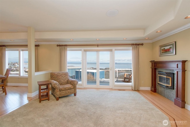sitting room with light wood-style flooring, ornamental molding, a glass covered fireplace, a water view, and baseboards