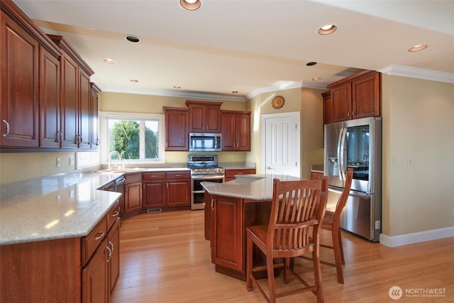 kitchen featuring light wood-style floors, a sink, ornamental molding, and appliances with stainless steel finishes